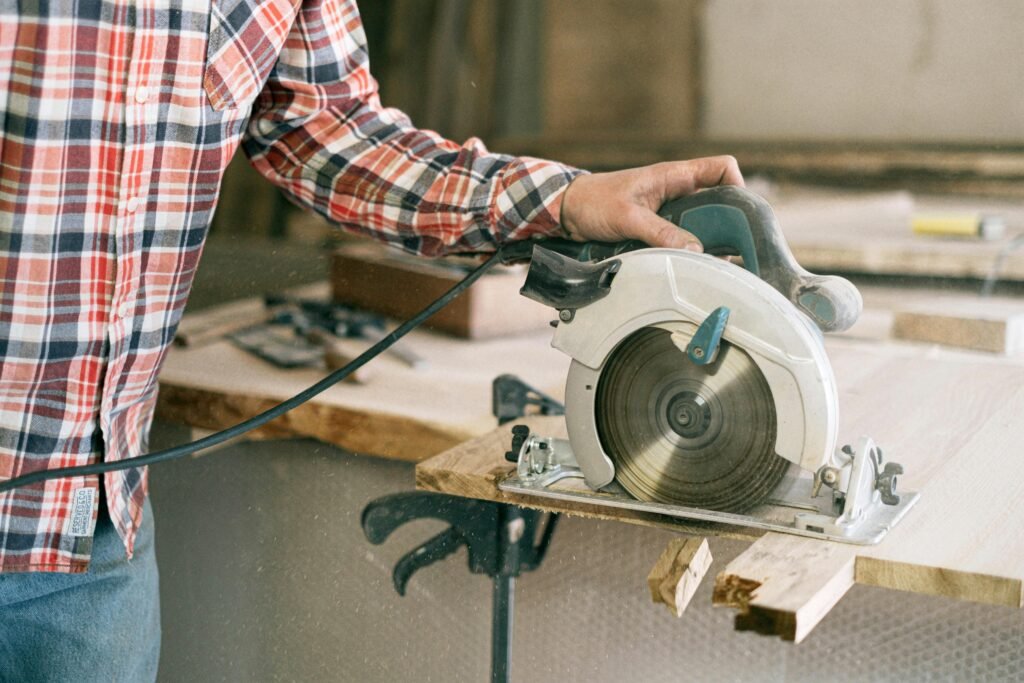 A carpenter in a plaid shirt uses a circular saw in a workshop, showcasing craftsmanship.